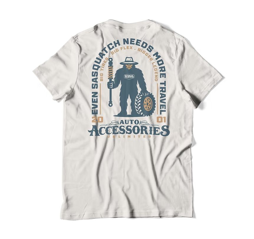 White T-shirt with a vintage tow truck graphic and NEEDS MORE TRAVEL and AUTO ACCESSORIES text.