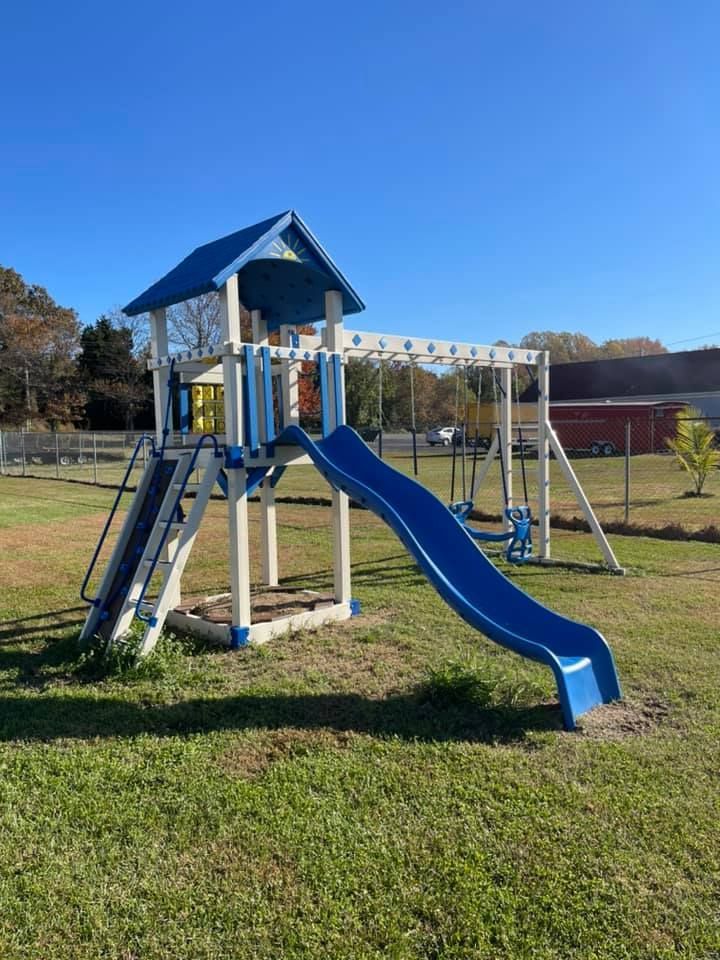 A blue and white playground set with a slide and swings in a grassy field.