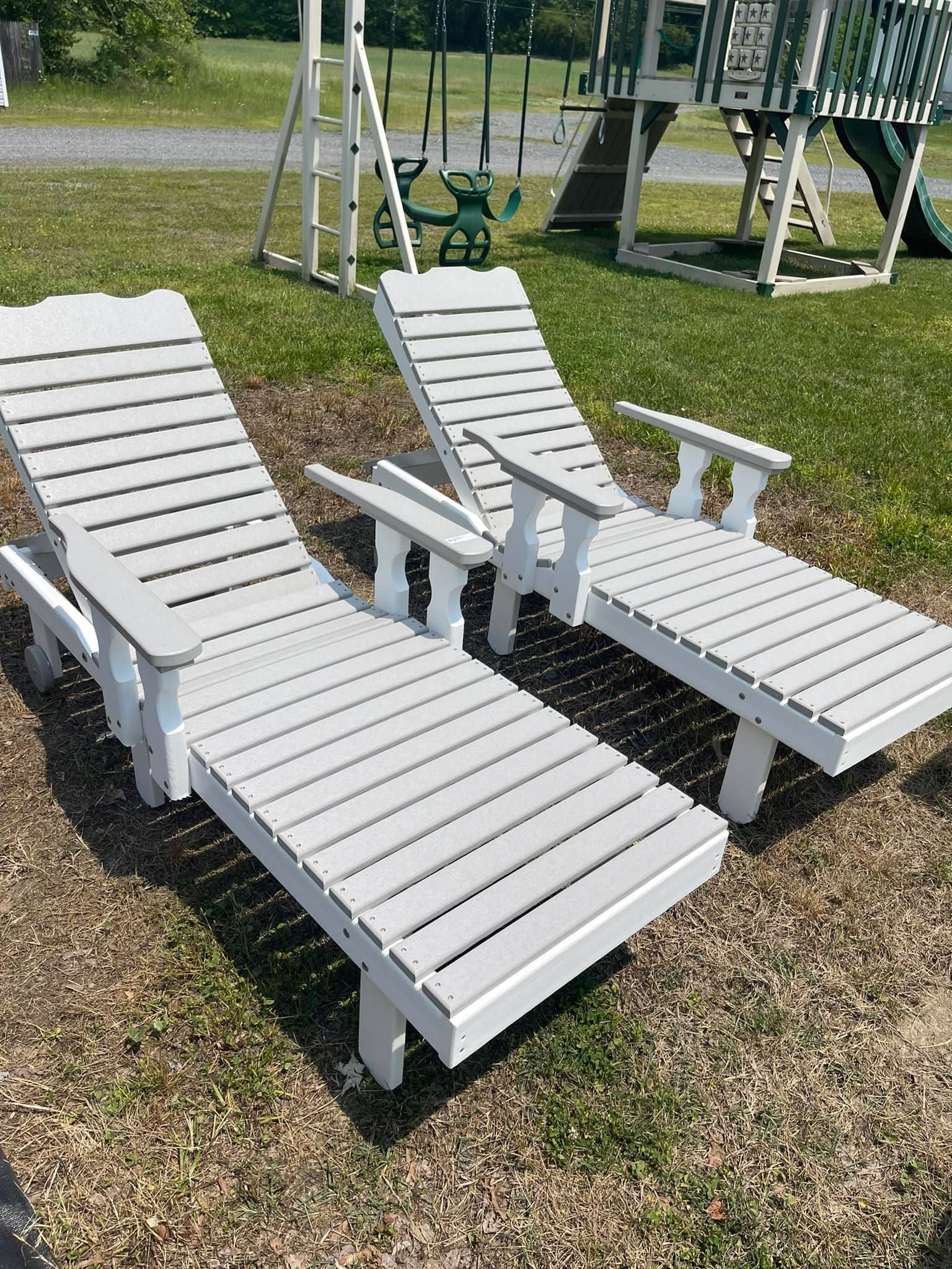 Two white lounge chairs are sitting in the grass in front of a playground.