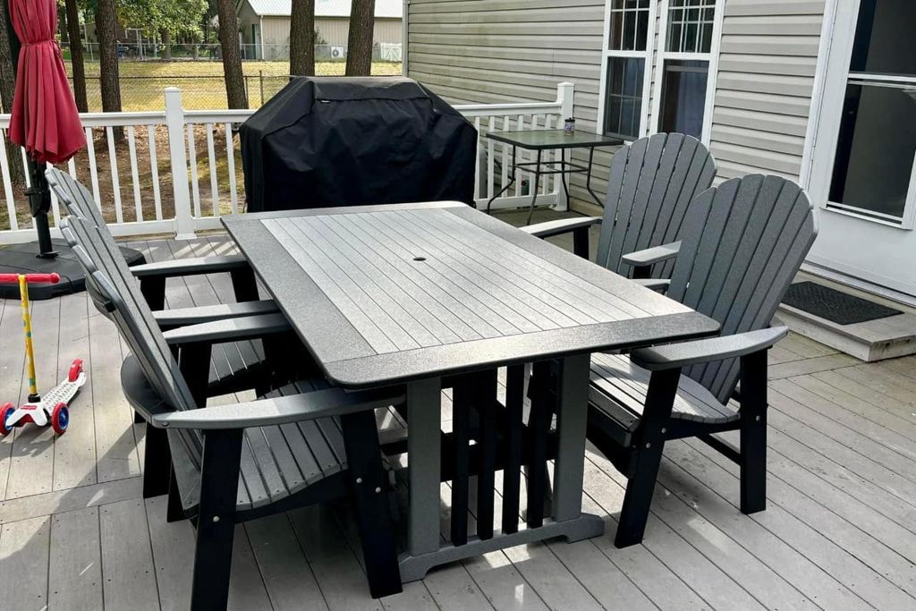 A table and chairs are on a deck next to a grill.