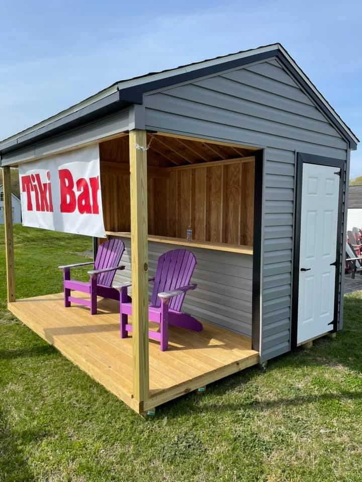 A tiki bar made out of a shed with purple chairs and a sign that says tiki bar.