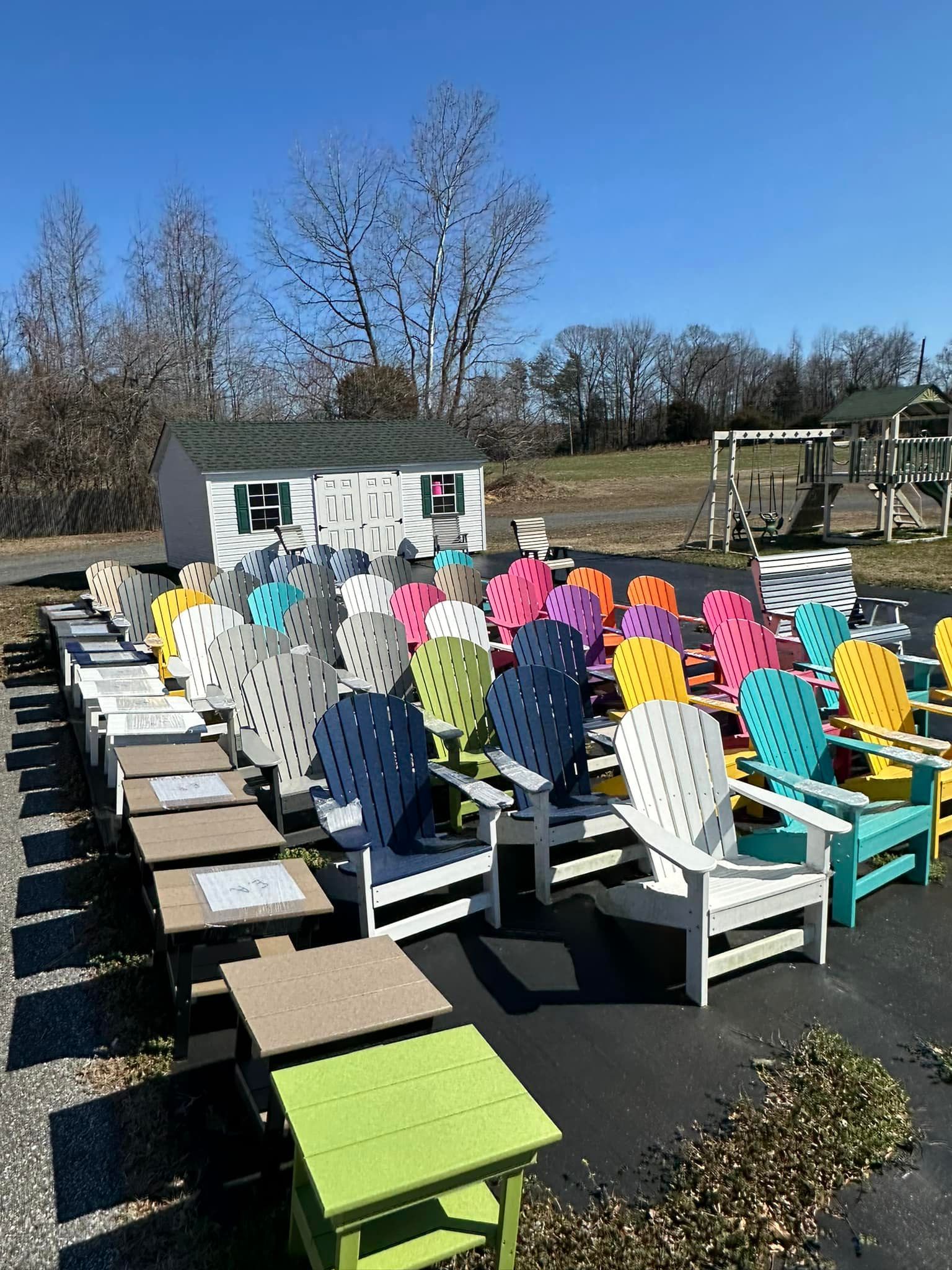 A row of colorful adirondack chairs and tables in a parking lot.