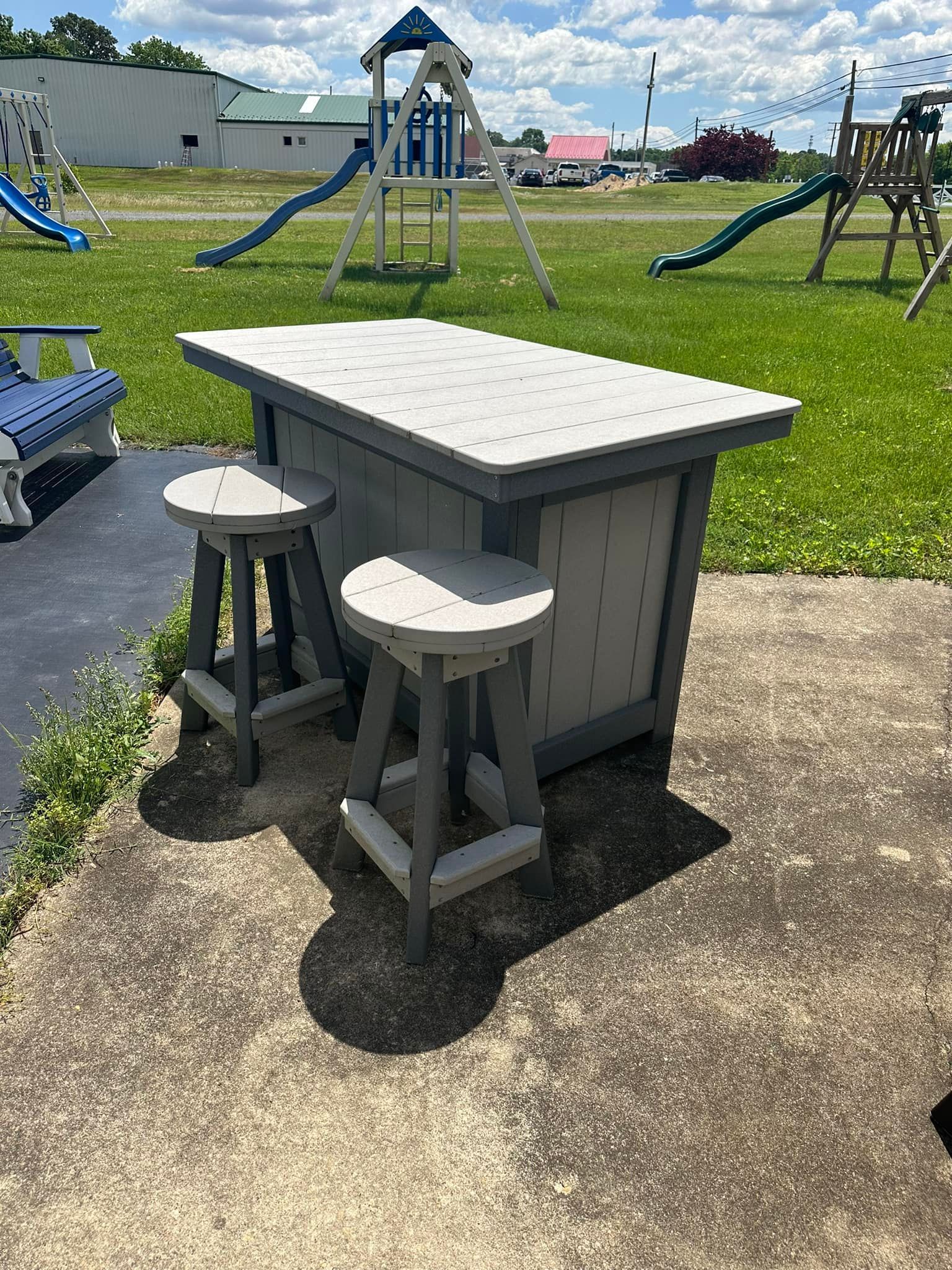 A table with two stools is sitting on a sidewalk in front of a playground.