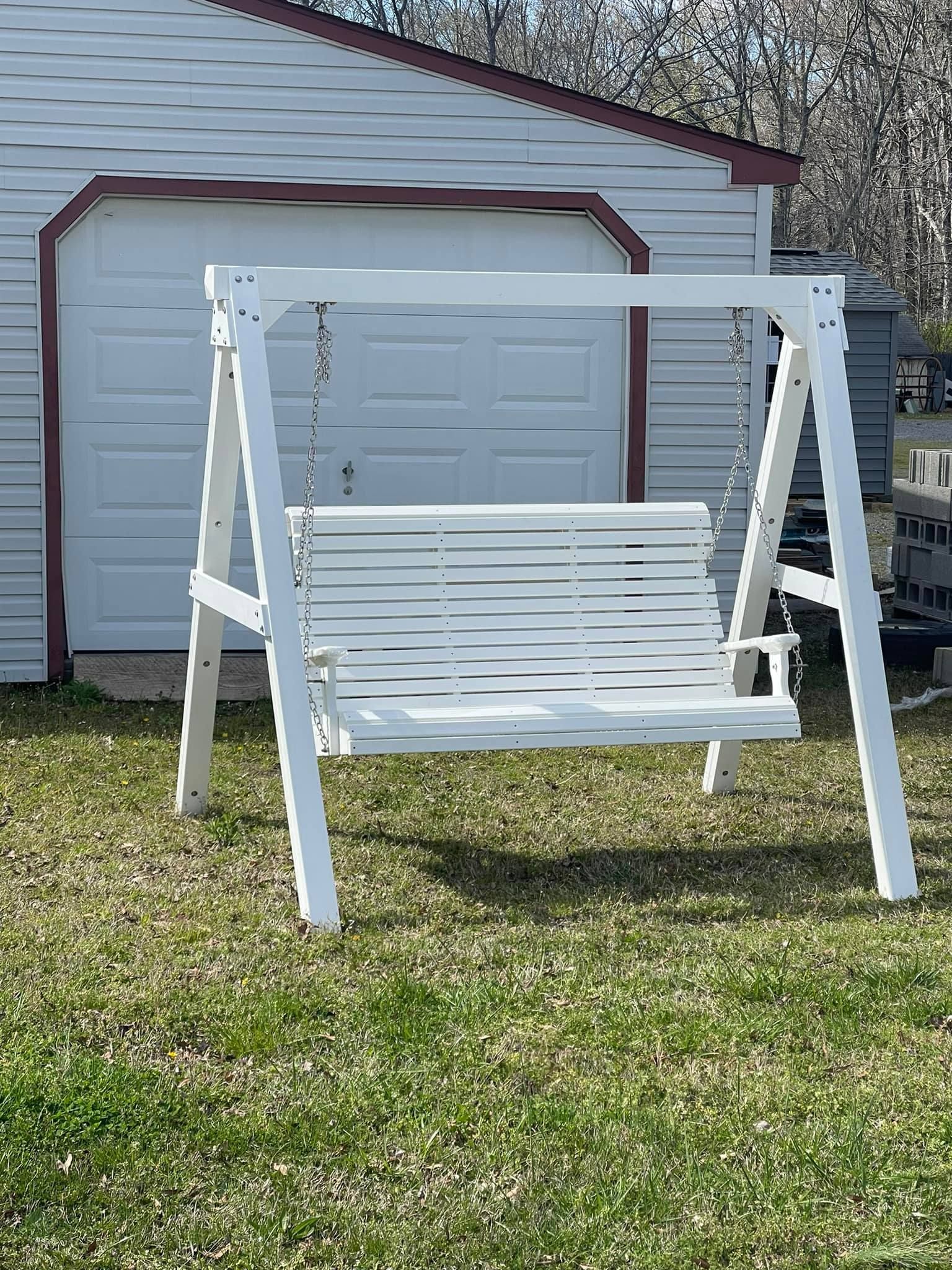 A white wooden swing is sitting in the grass in front of a garage.