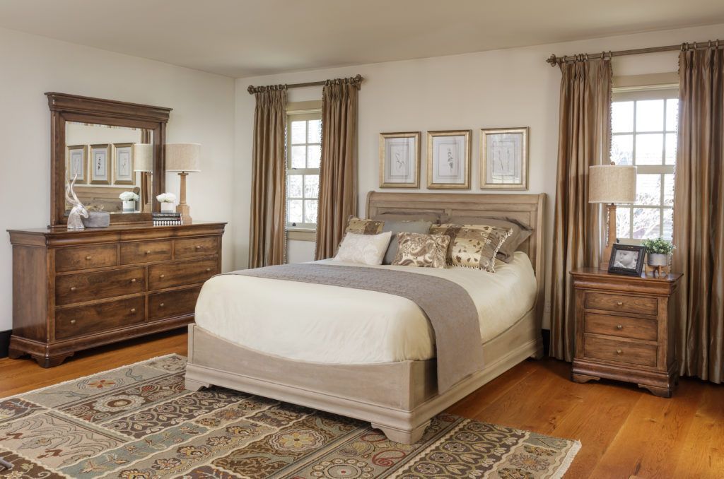 A bedroom with a bed , dresser , nightstand , mirror and rug.
