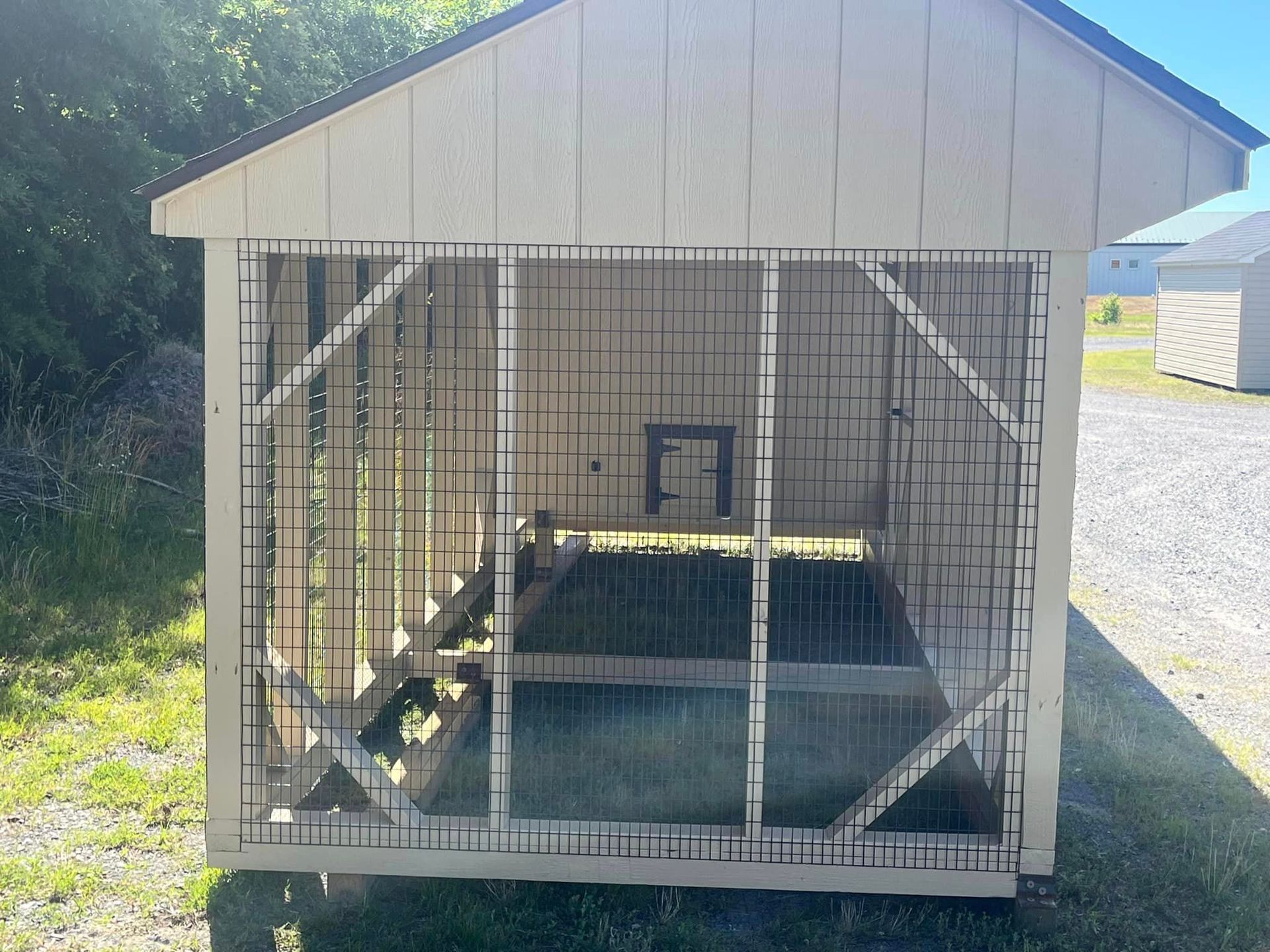 A white shed with a black roof is sitting in the grass.