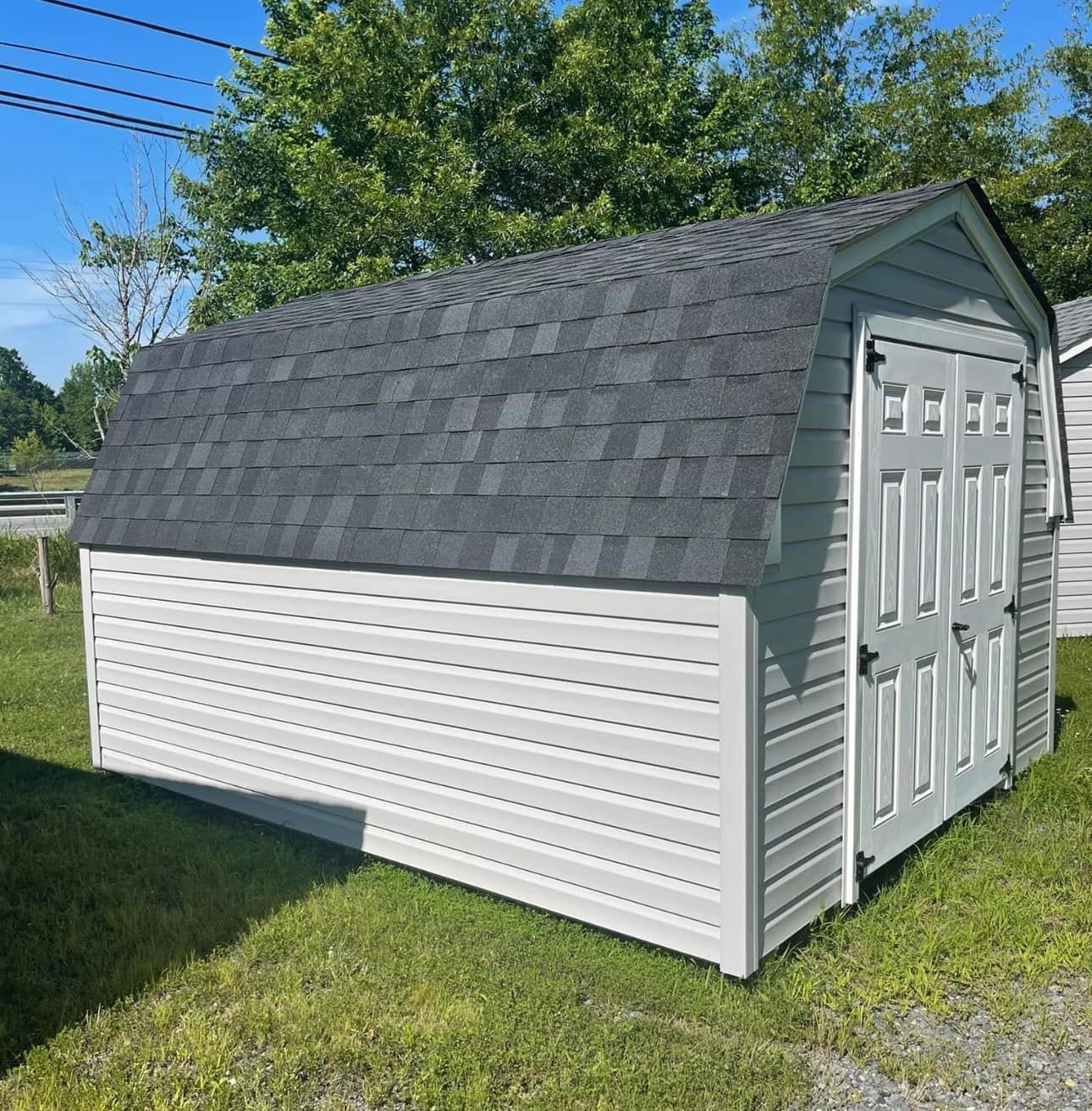 A white shed with a black roof is sitting in the grass.