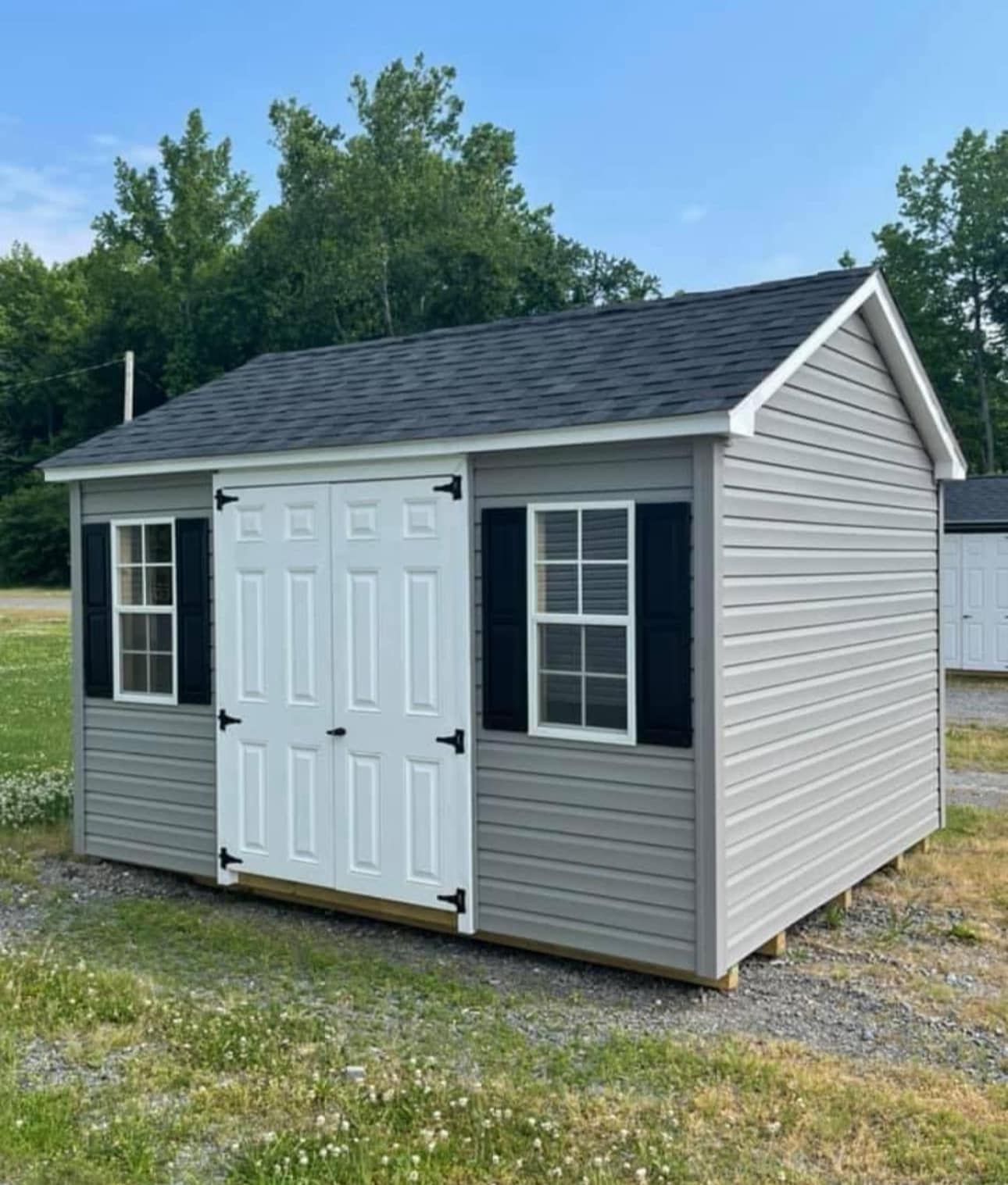 A small gray shed with black shutters is sitting in the middle of a grassy field.