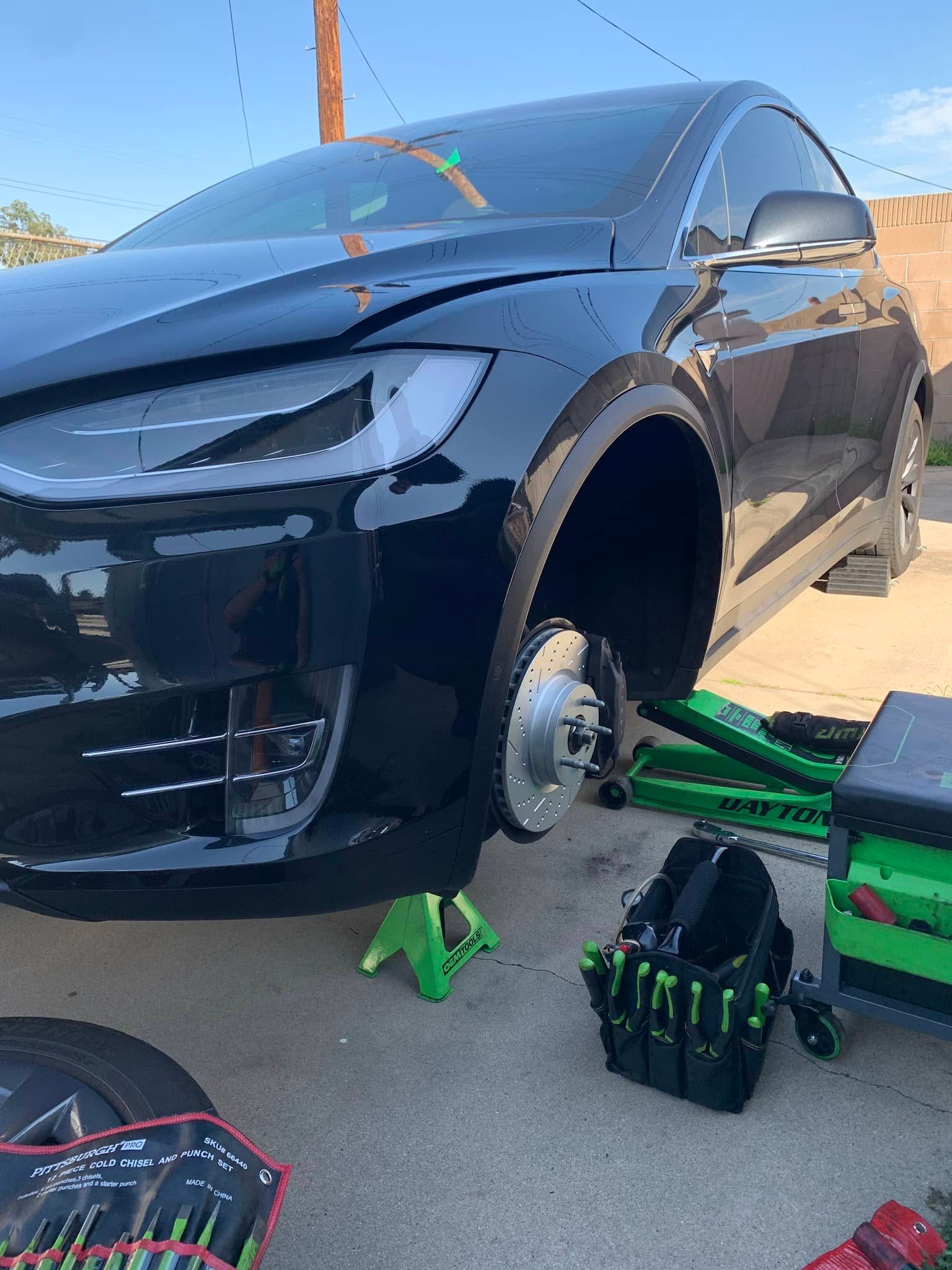Black Tesla SUV raised on jack stands; front tire removed.