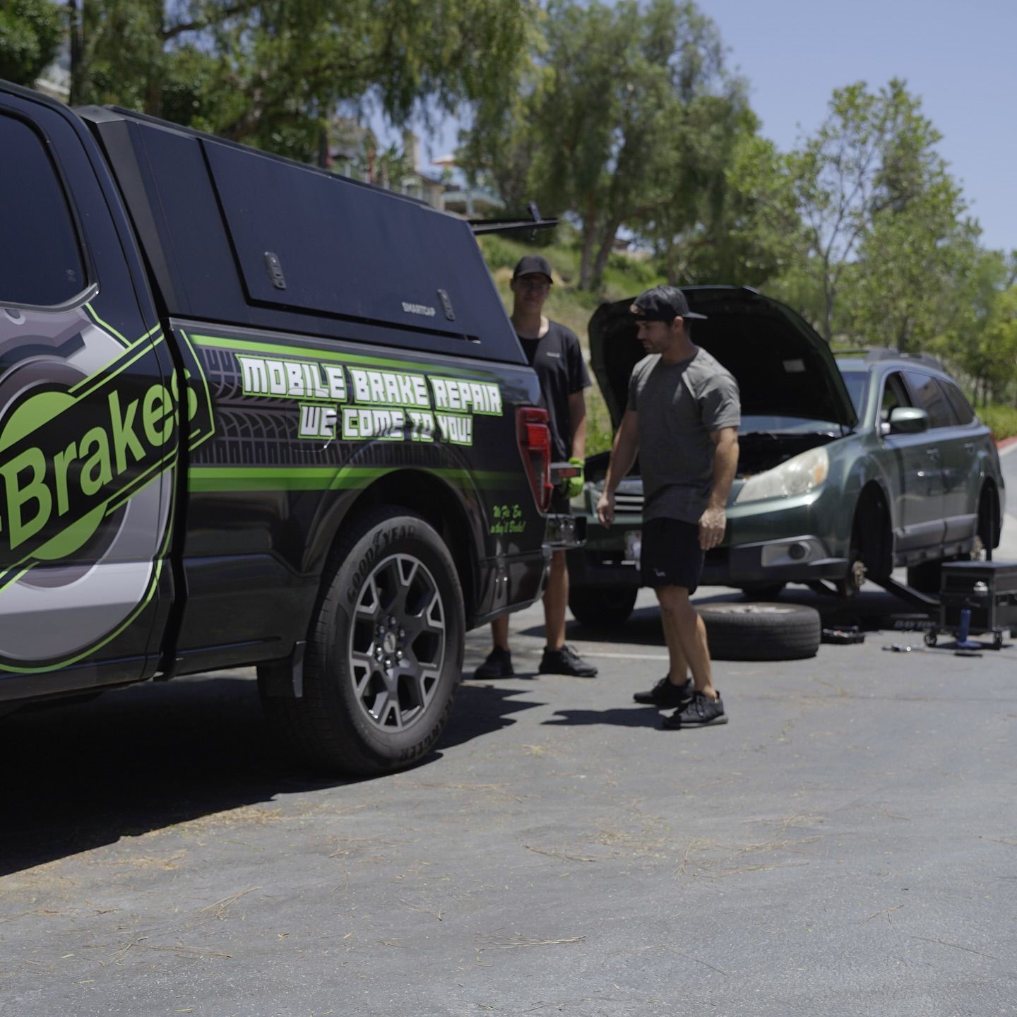 Mobile Brake Repair truck servicing a car; two men working outdoors with the hood open and a tire off.