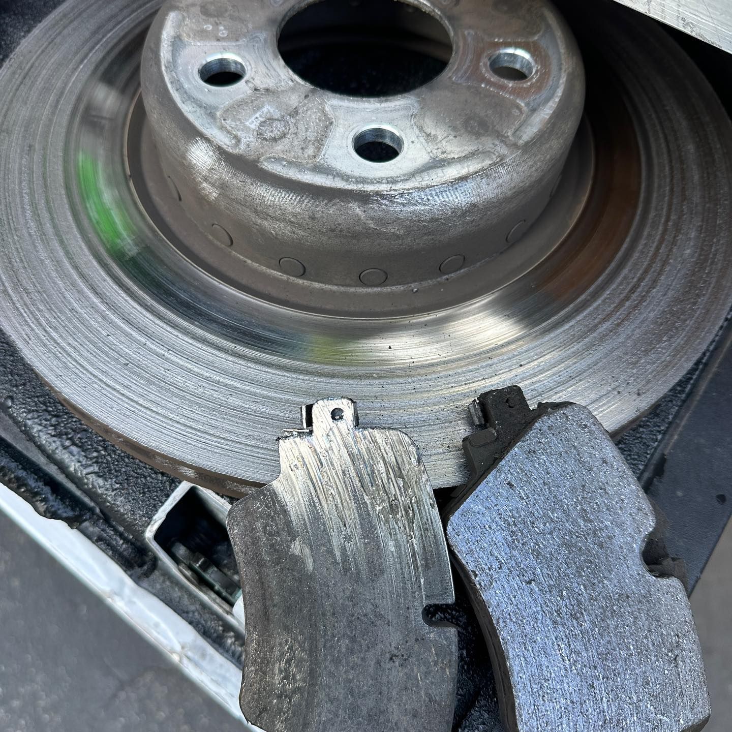 Brake rotor and worn brake pads, metallic gray, lying on a surface, likely during car repair.