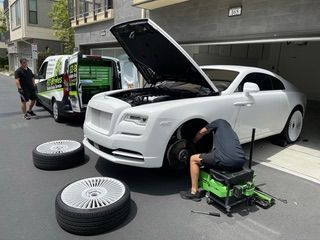 Mechanic changing tire on a white Rolls Royce with service van.