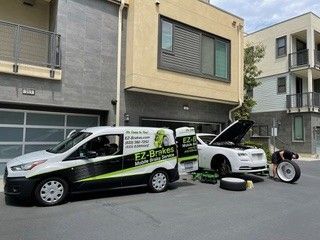 EZ Brakes mobile service van near a white car with an open hood a person changing a tire.