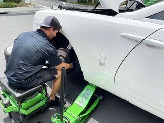 Mechanic working on the front tire of a white Rolls Royce, using a green jack.