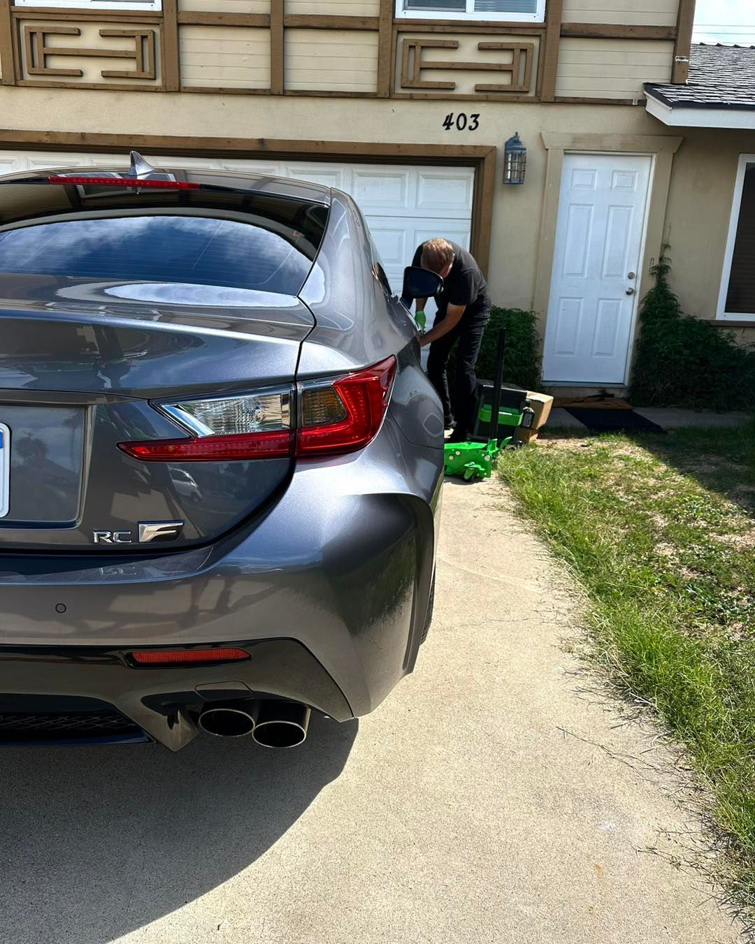 Gray sports car parked on a driveway with a person working on it in front of a house.
