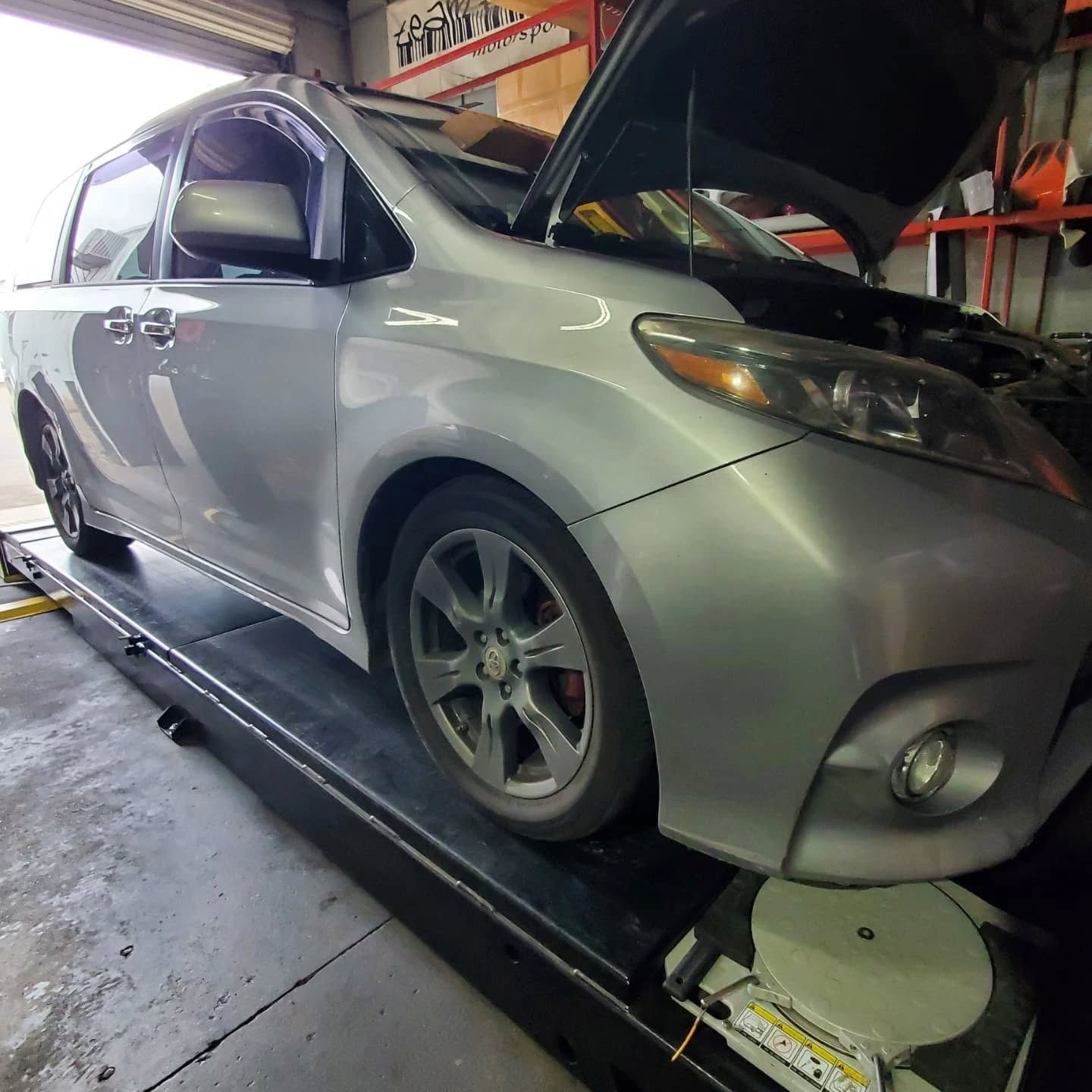 Silver car on a dynamometer in a garage, hood open during maintenance or inspection