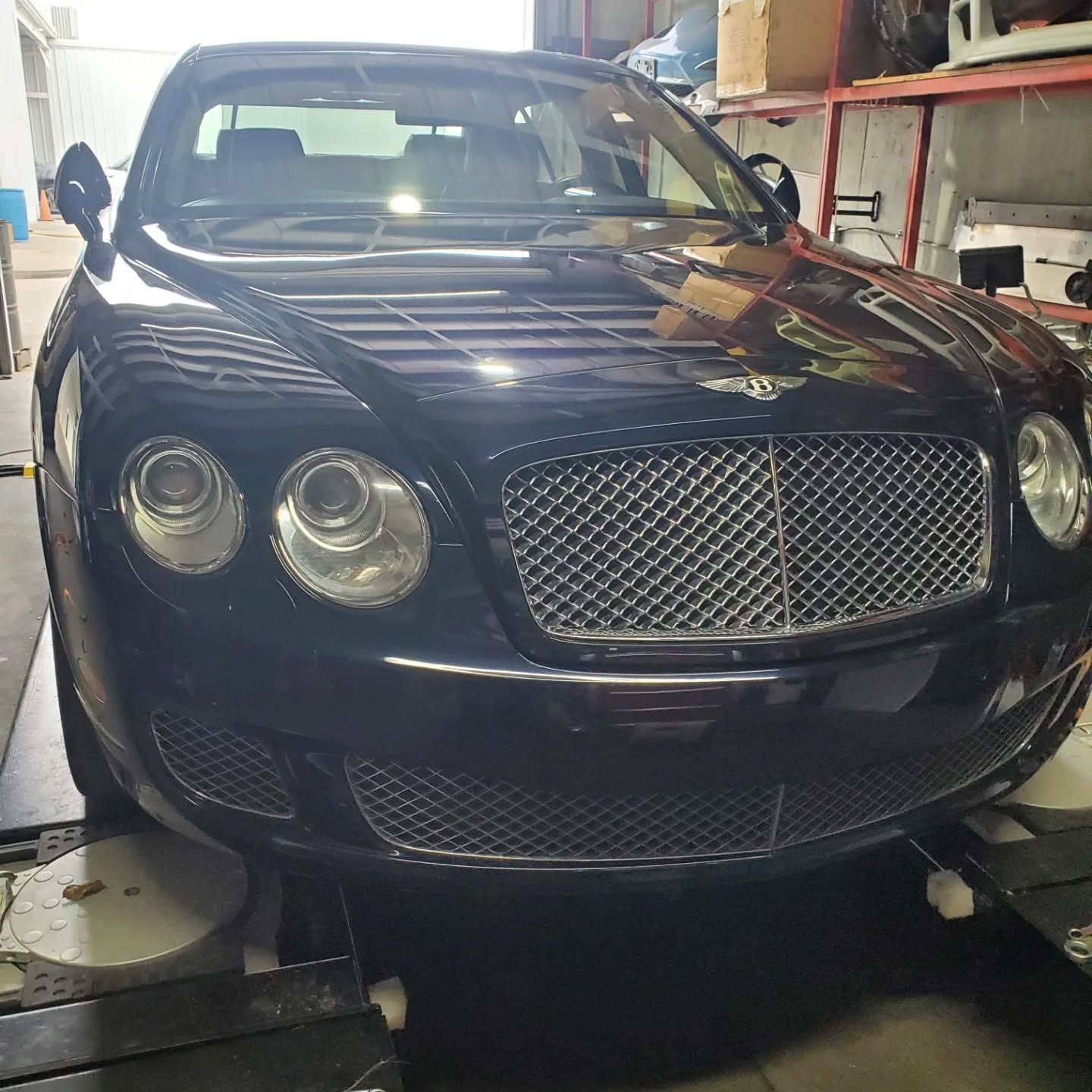 Dark blue Bentley sedan in a garage, front view, with chrome grille and round headlights.