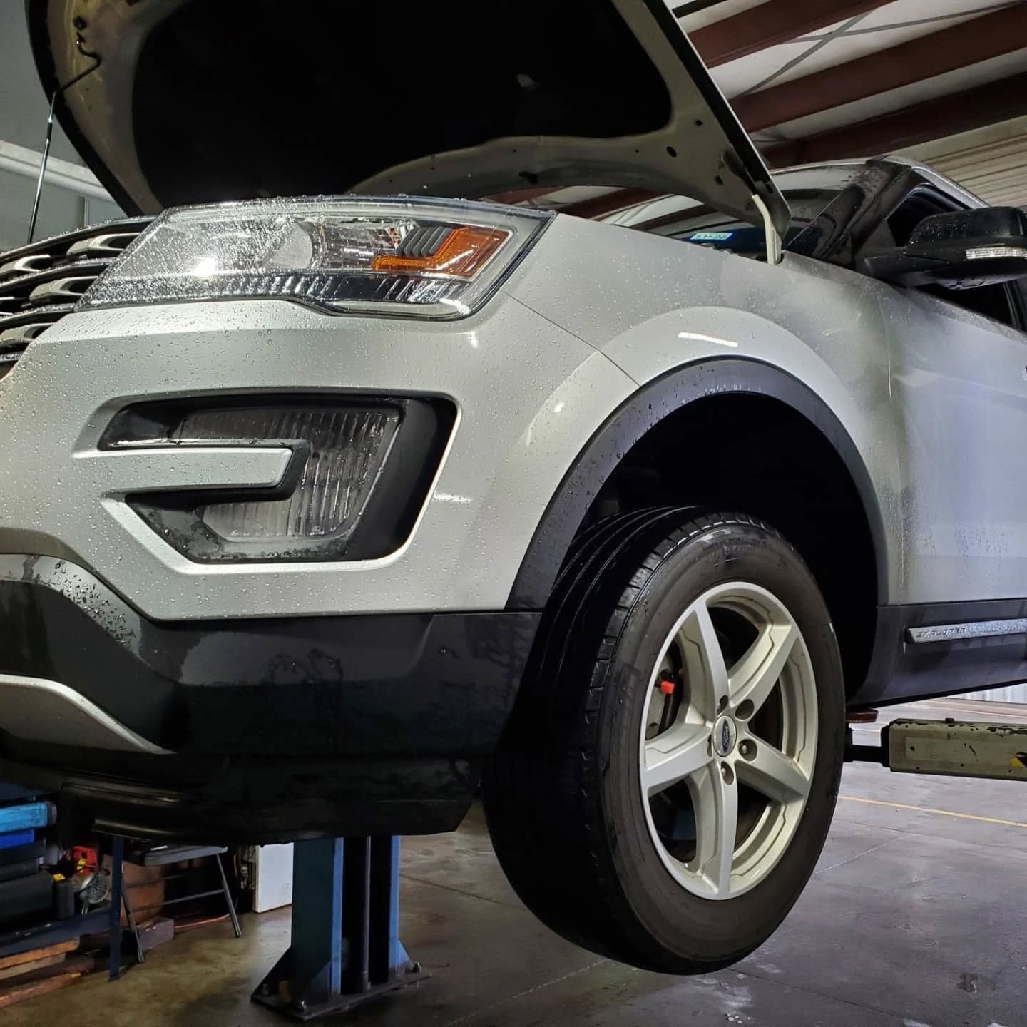 White SUV on a lift in an auto repair shop with hood open and front wheel raised