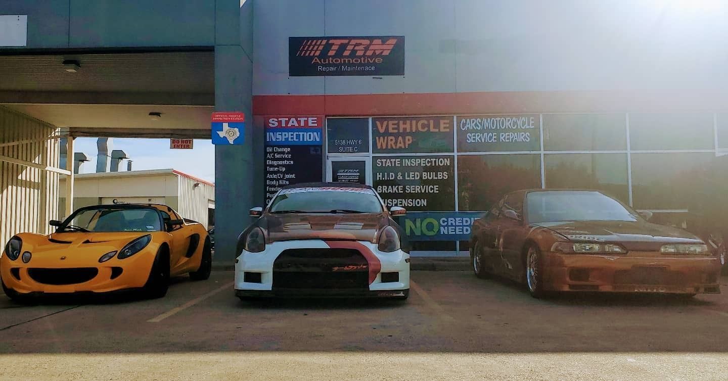Three modified sports cars parked outside a car shop, including an orange coupe and a brown sedan.