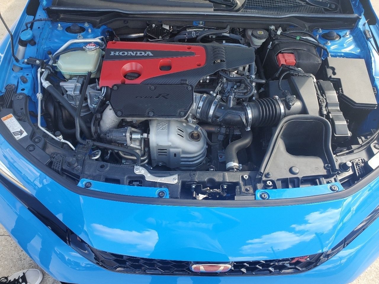 Blue car with open hood showing a modified engine bay and red engine cover