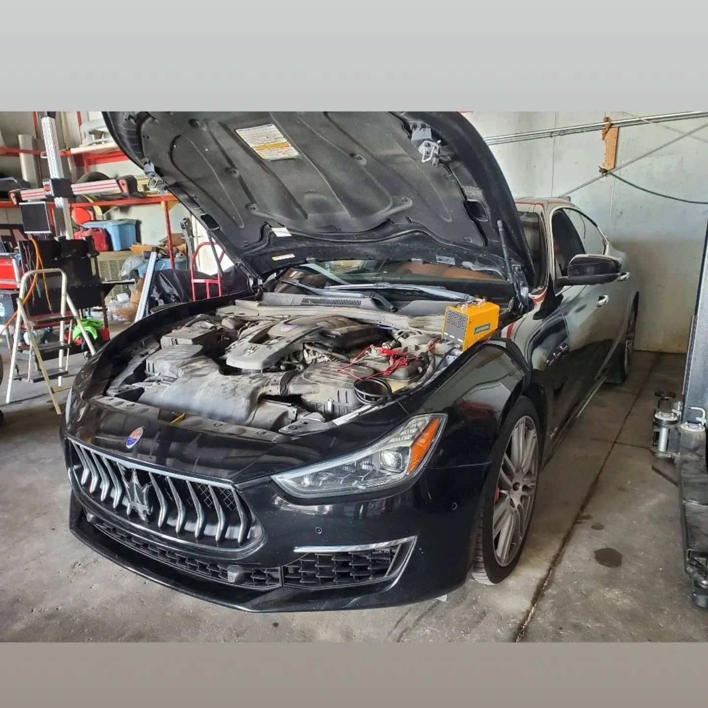 Black sedan with hood open in a garage, showing engine damage or repair work