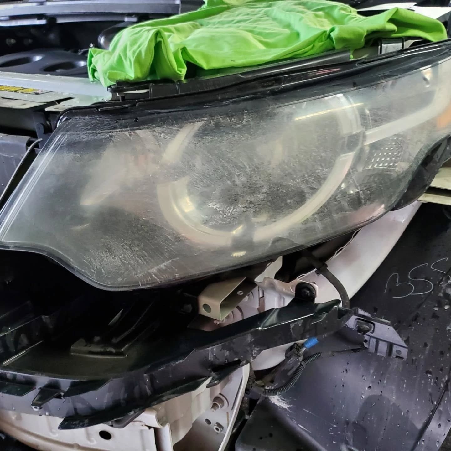 Damaged car headlight and front bumper with green cover draped over the hood