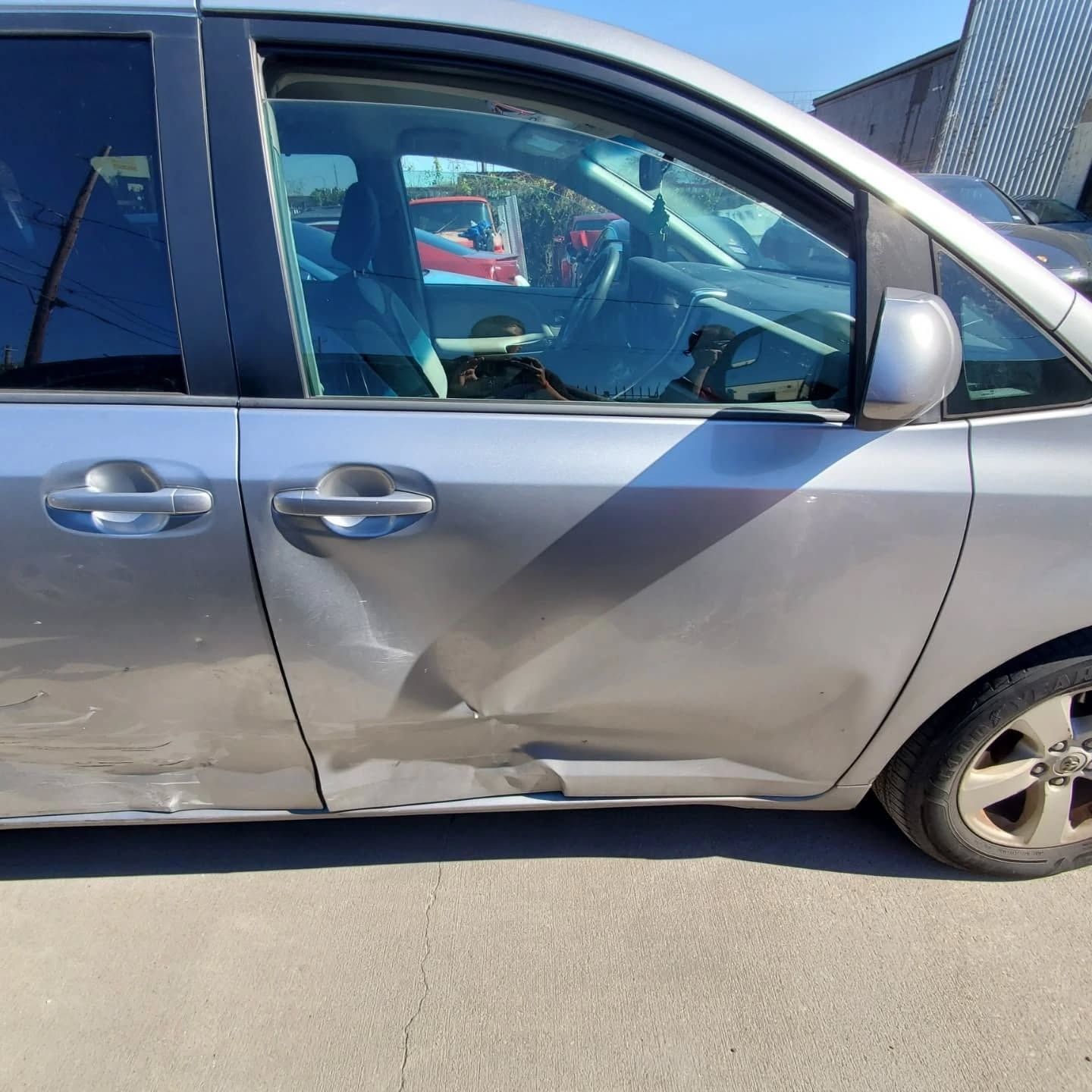 Silver minivan with a large dent and scrape on the side in a parking lot