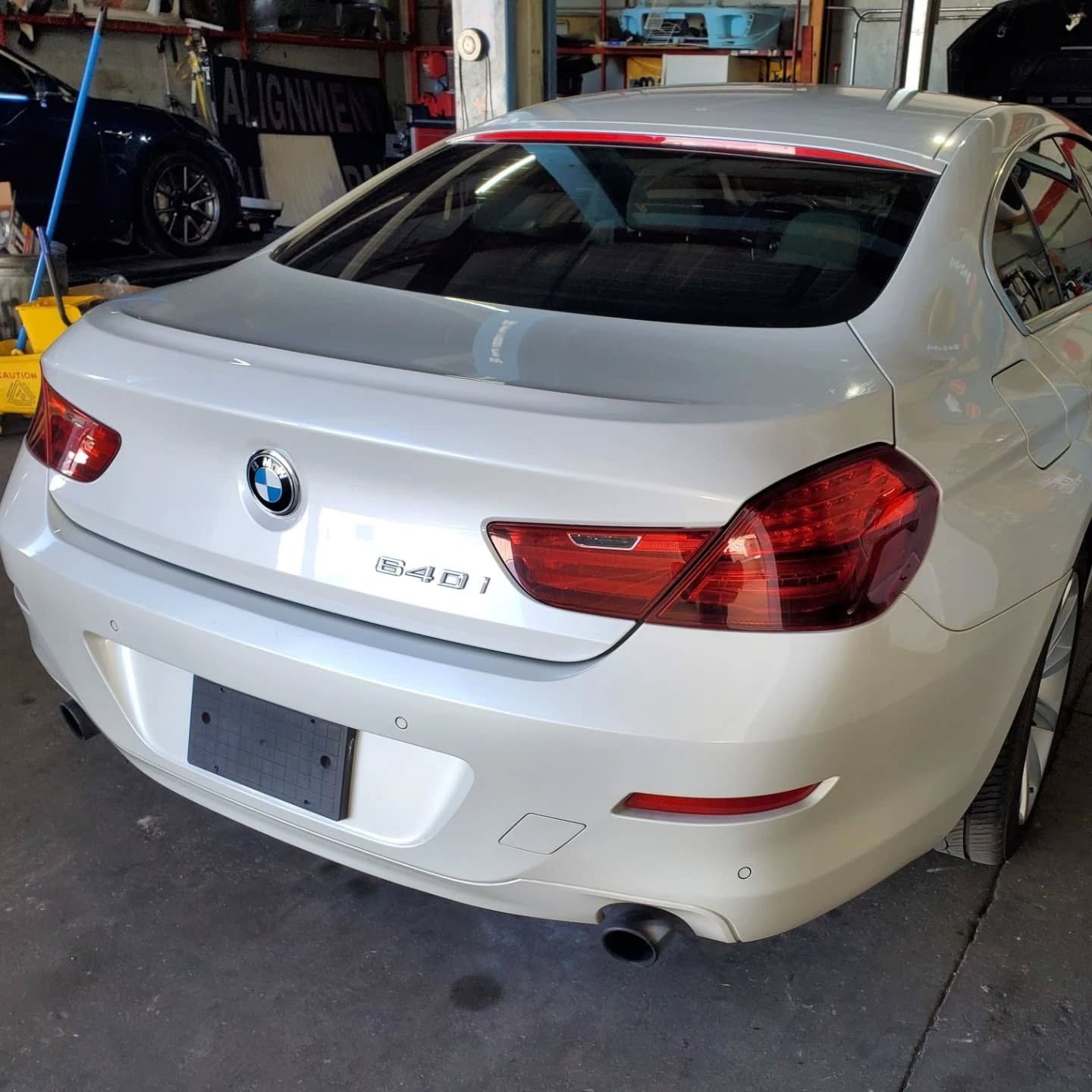 White BMW 640d coupe parked in a garage, rear view with taillights and exhaust visible