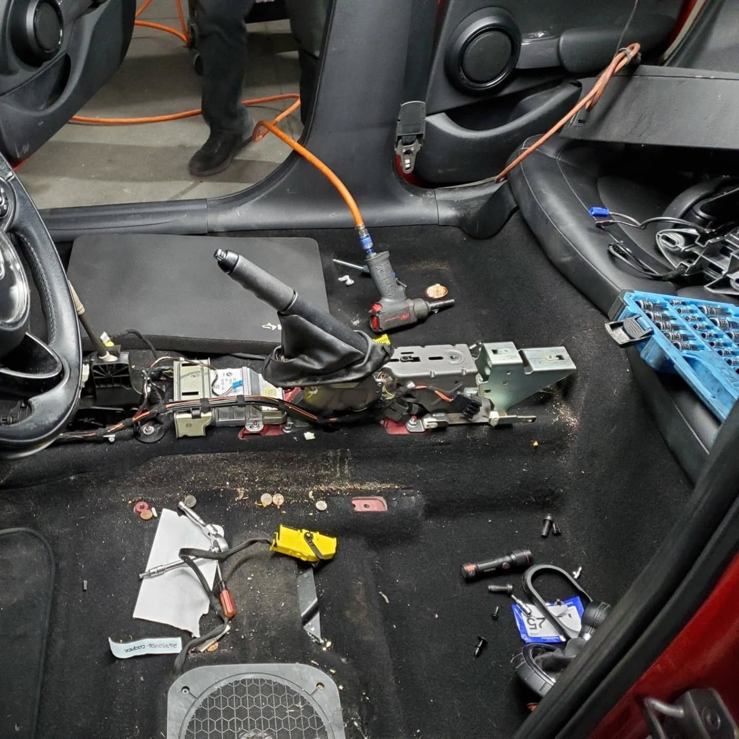 Car interior stripped for repairs, with exposed wiring, tools, and loose components on the floor.