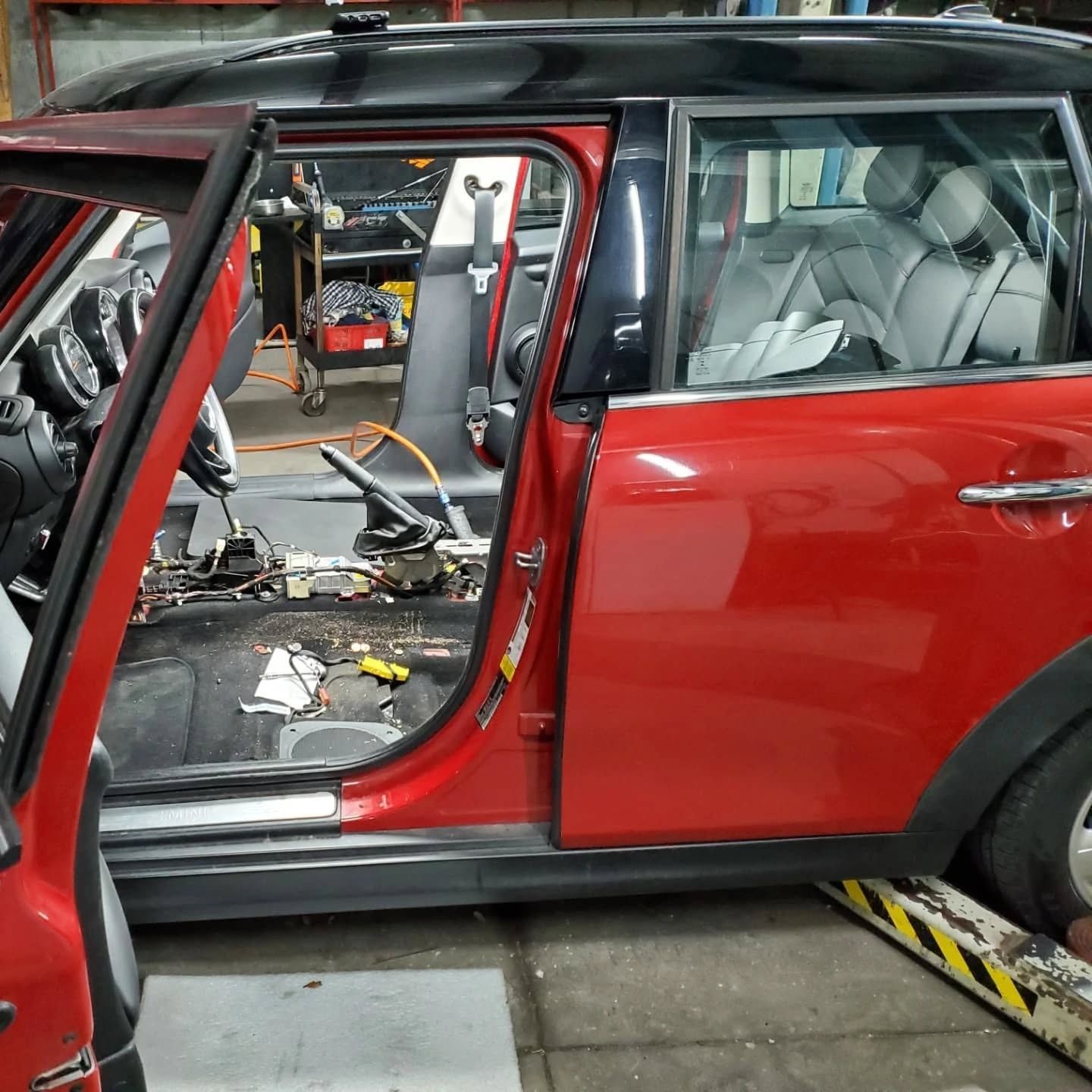 Red SUV with open door, showing a stripped interior during repair in a garage