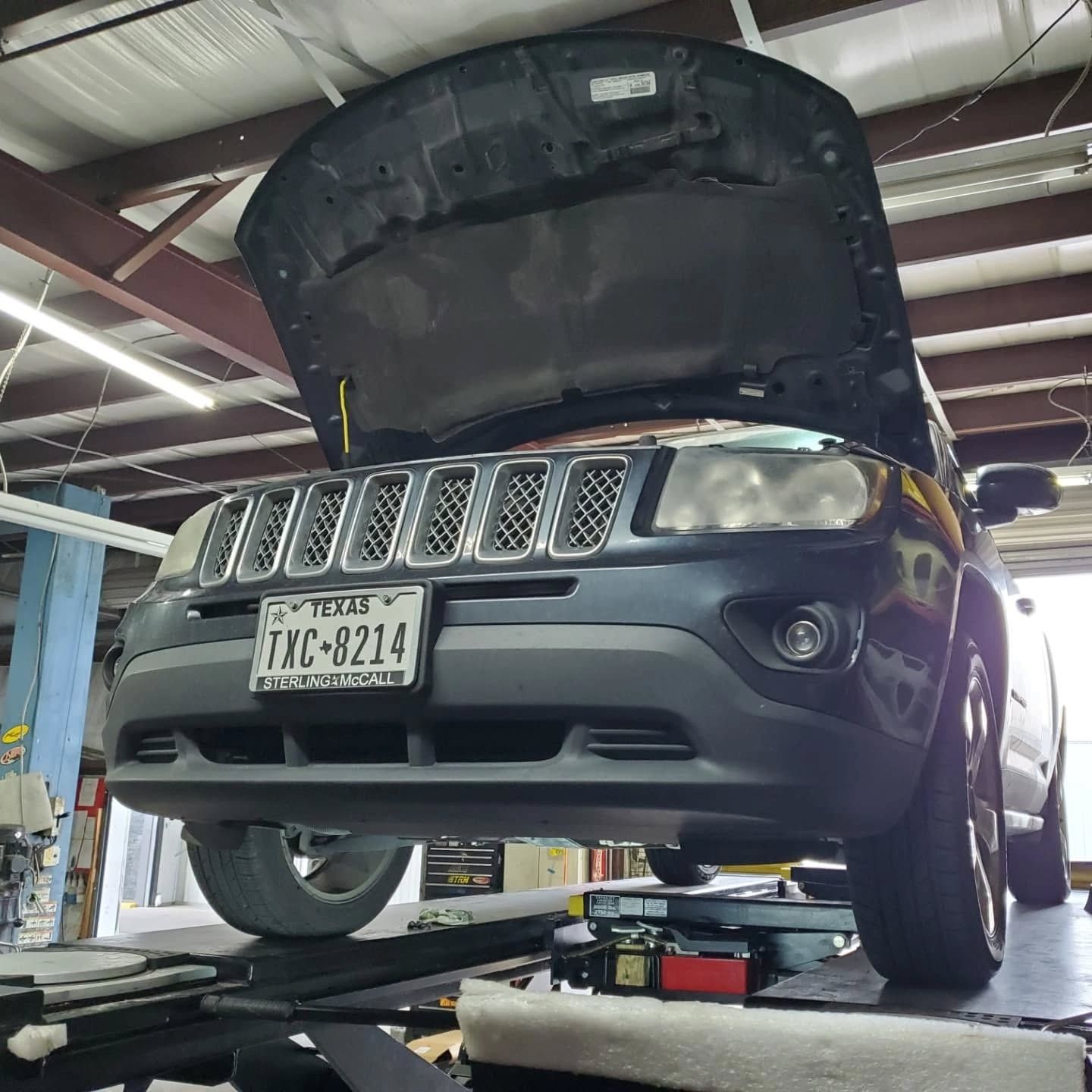 Gray SUV on a lift in an auto shop with its hood open, viewed from the front.