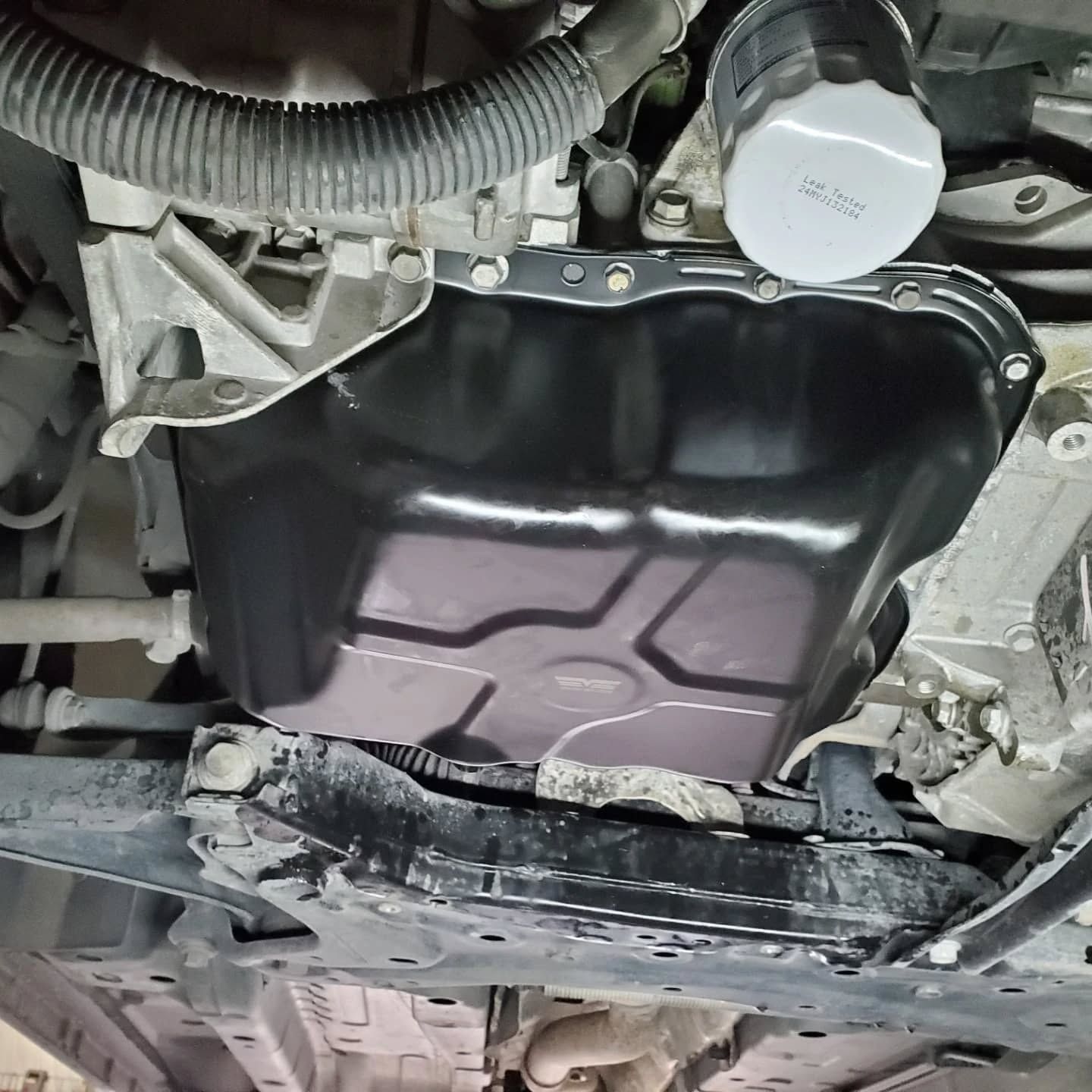 Underbody view of a car with the oil pan removed, exposing the engine underside and drain pan area