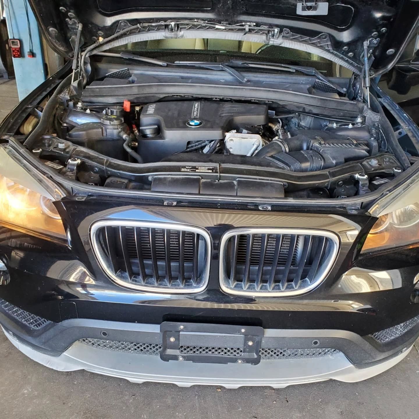 Black BMW with hood open in a garage, showing the engine bay and front grille.