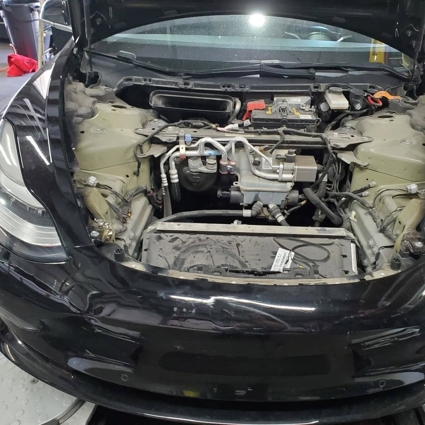 Black sports car with front bumper removed, exposing the engine bay in a workshop