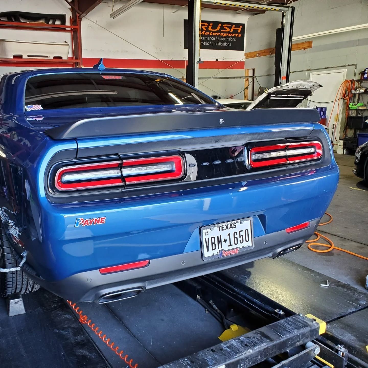 Blue Dodge Challenger on a dynamometer in a garage, rear view with taillights lit.