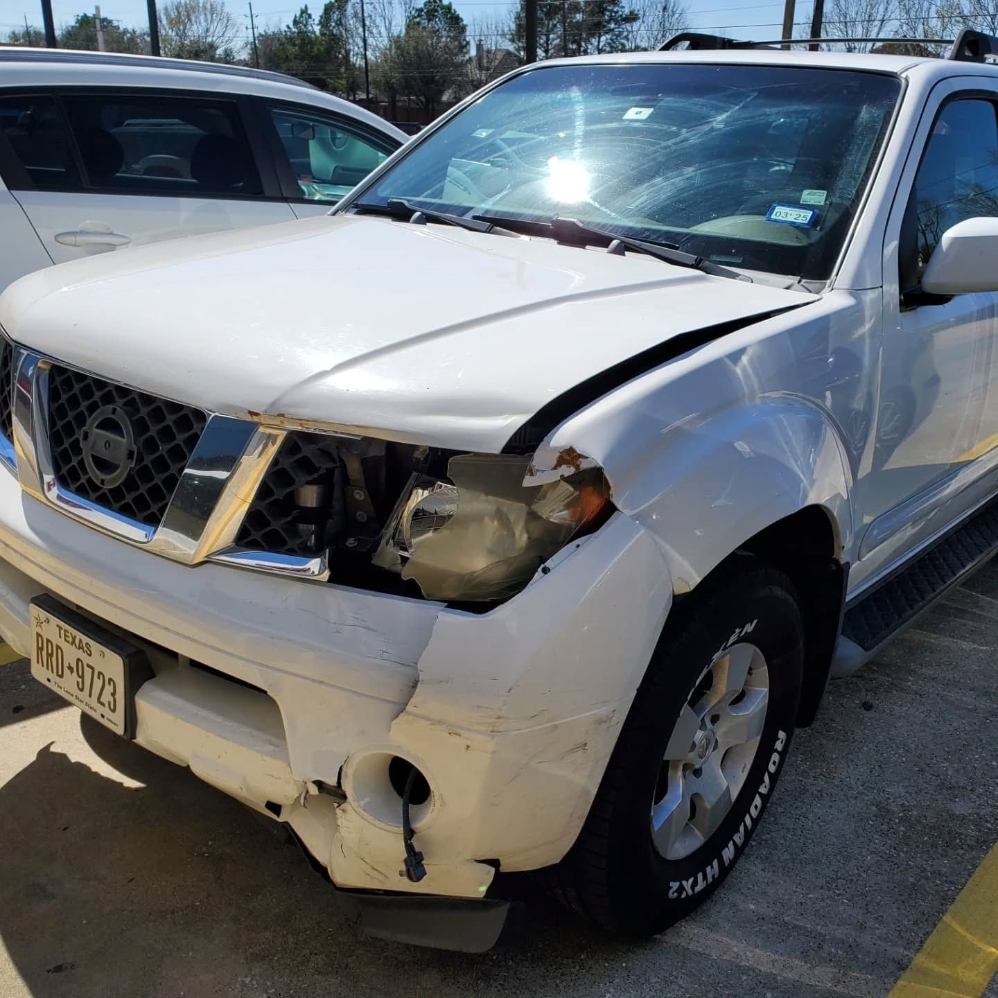 White SUV with front-end collision damage, broken headlight, and crumpled bumper in a parking lot