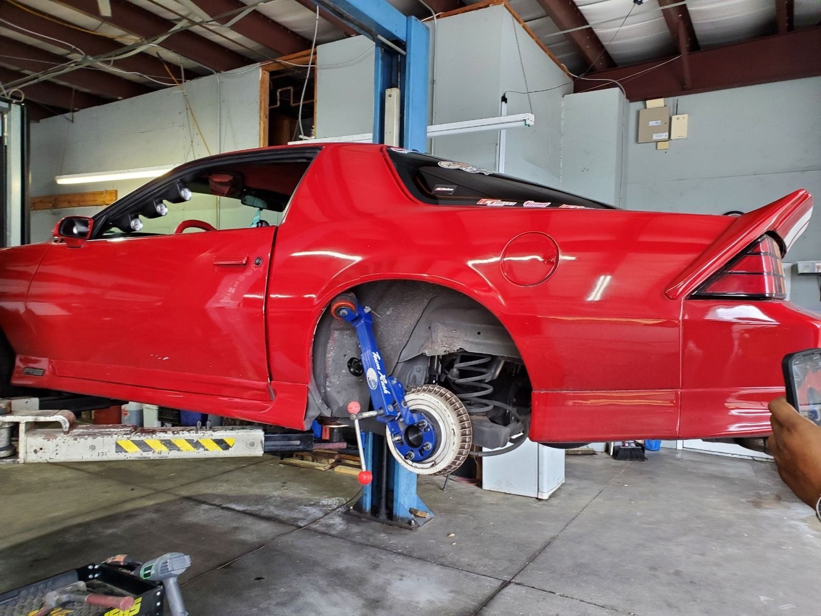 Red sports car lifted on a shop hoist with the rear wheel removed, inside a garage