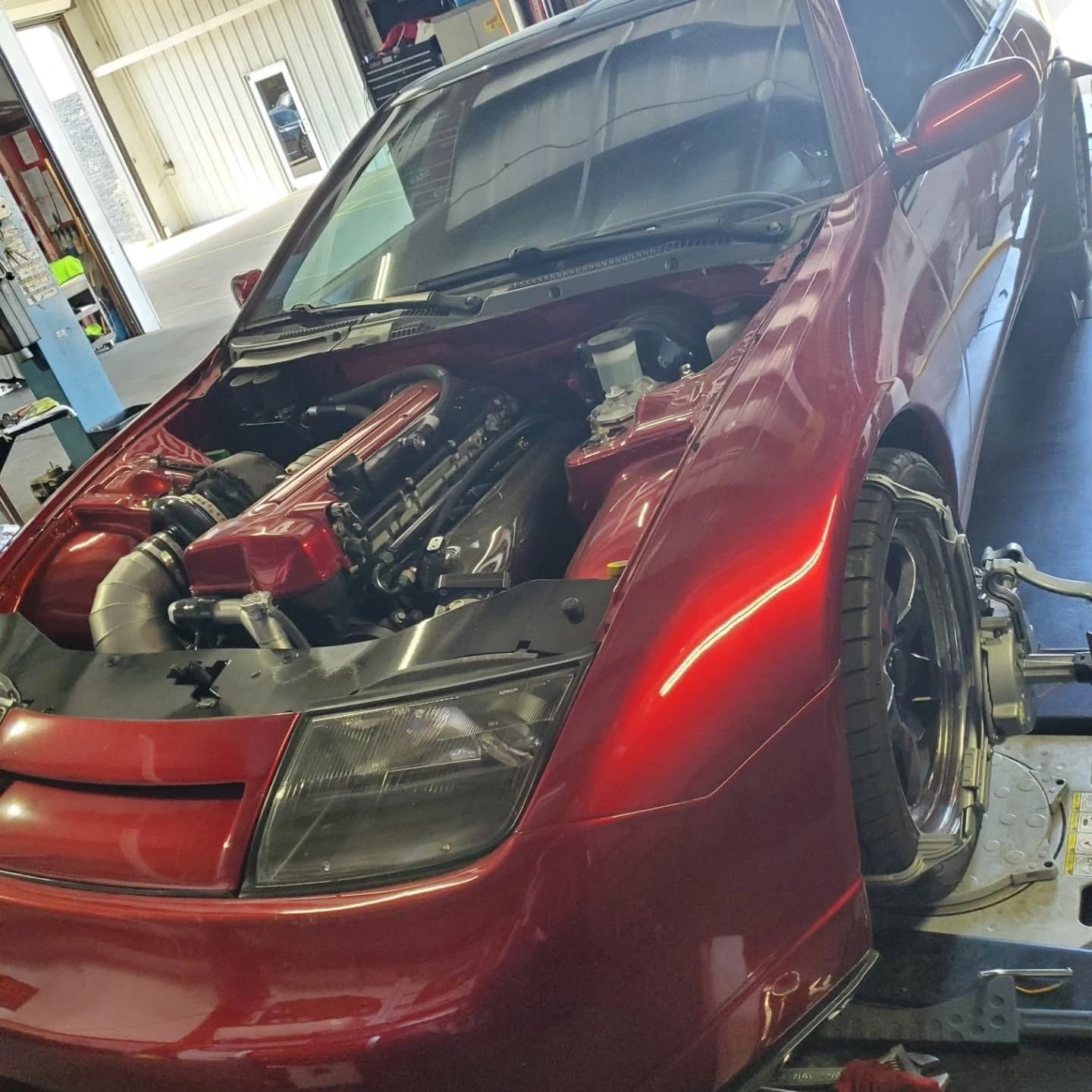 Red car in a garage with hood open, showing engine modifications and front bumper removed