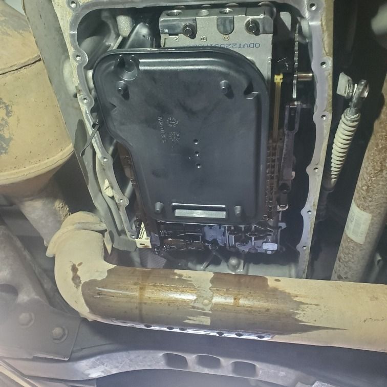 Undercarriage view of a vehicle showing a black transmission pan and rusted exhaust pipe underneath.