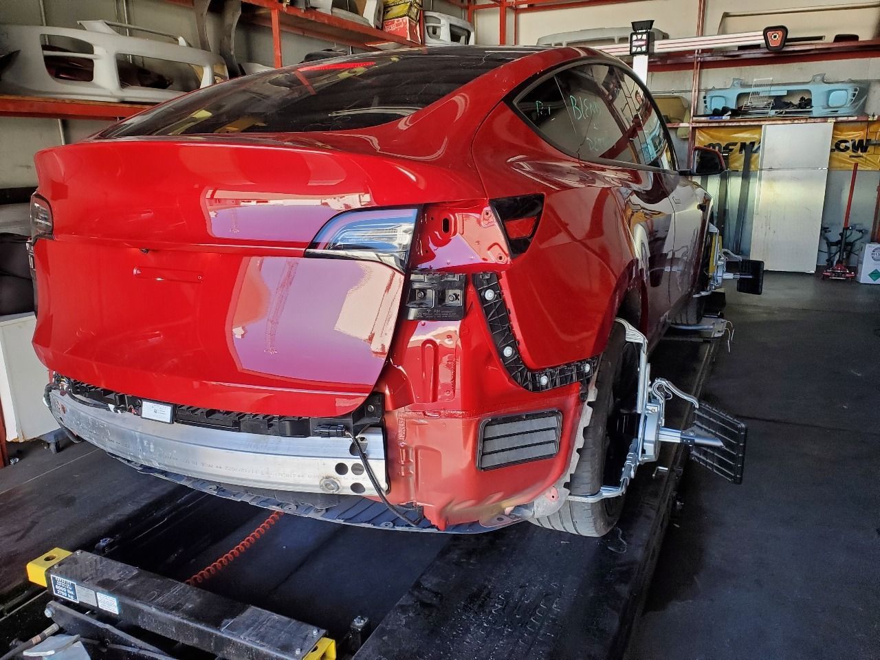 Red sports car with rear body damage inside an auto repair shop on a lift