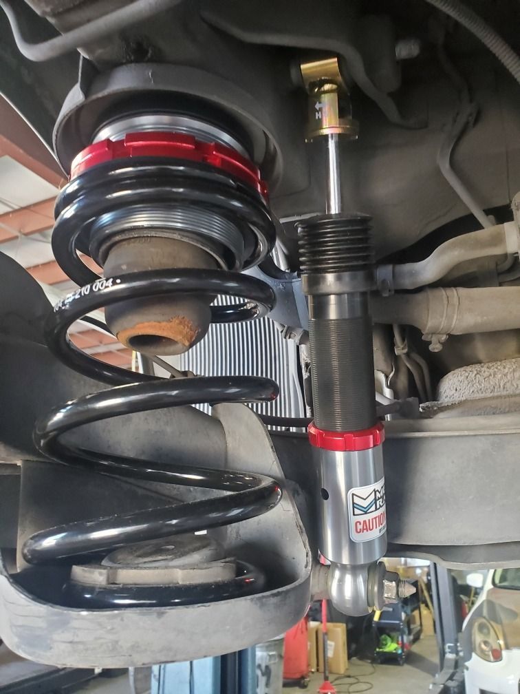Coilover suspension and spring assembly under a vehicle, with a black spring and red adjustment ring.