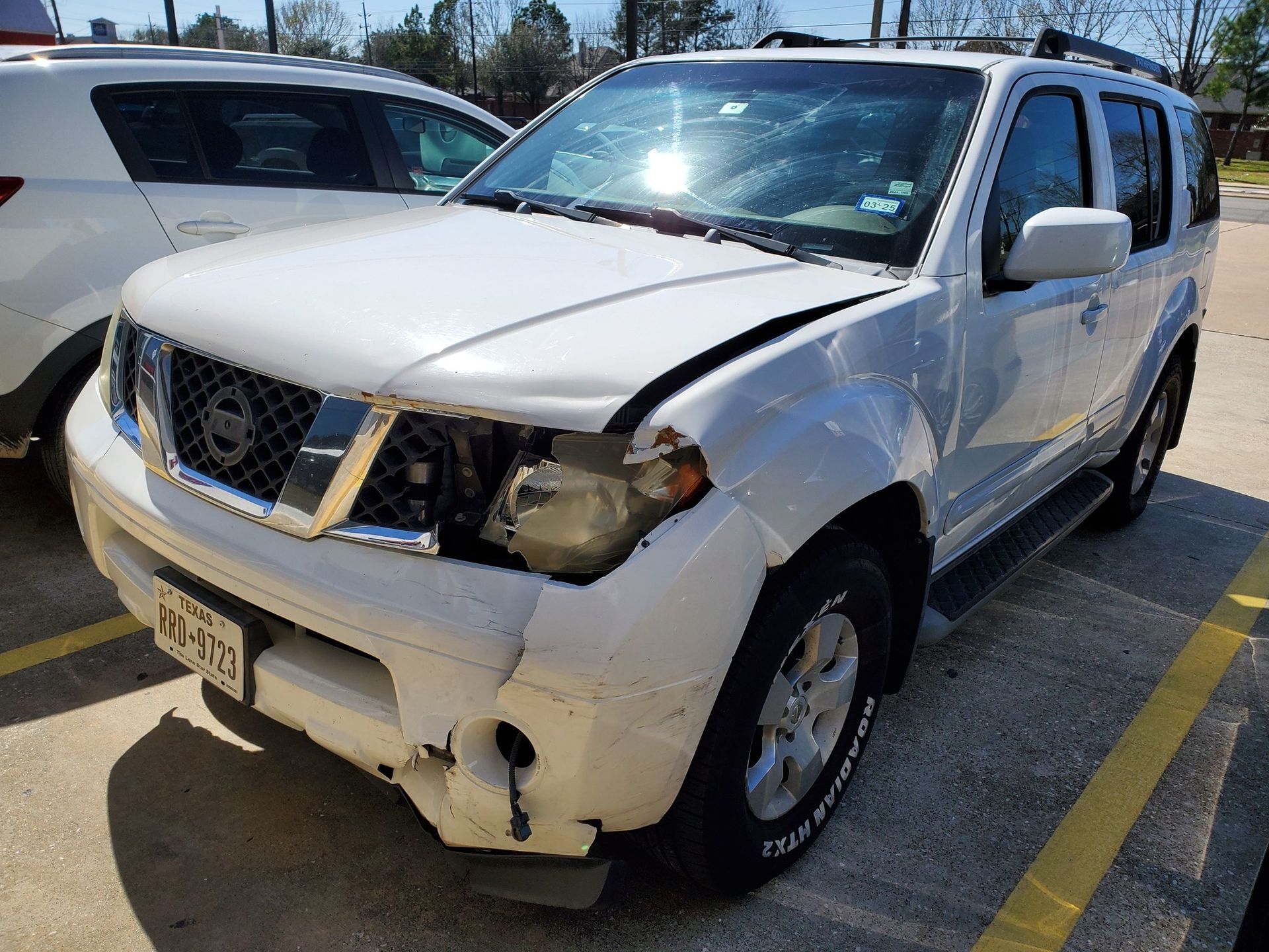 Damaged white SUV with a crumpled front end, parked in a lot after a collision
