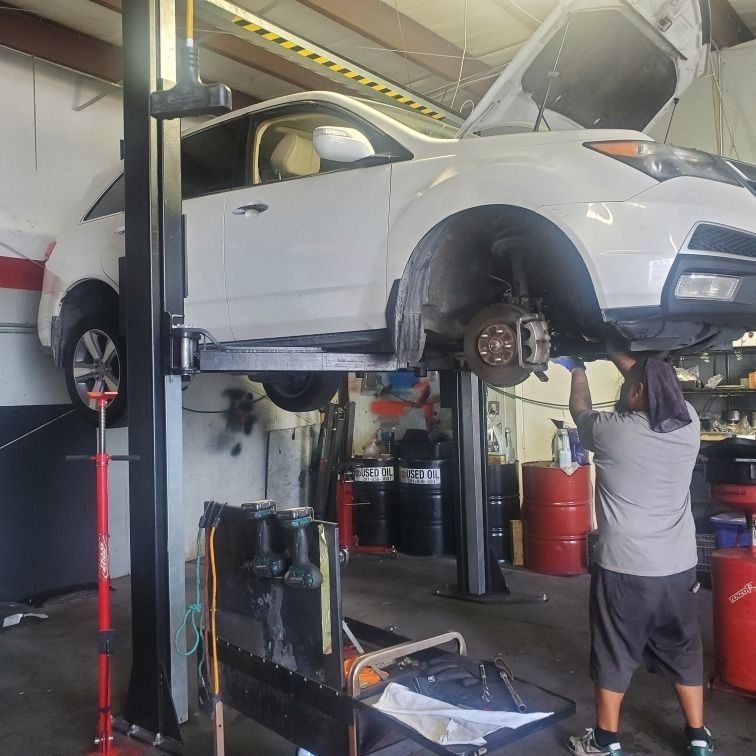 White SUV lifted on a garage hoist while a mechanic works on the front wheel area in an auto shop