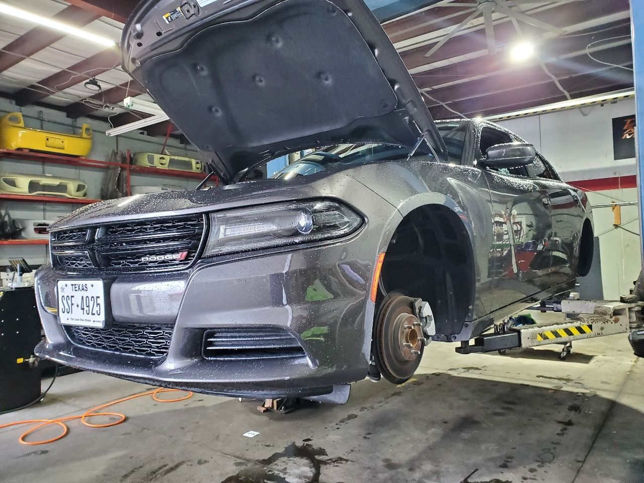 Gray car lifted in an auto shop with hood open and front wheel removed for repair
