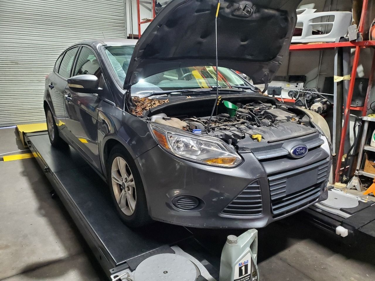 Gray Ford sedan with hood open on a lift in an auto repair shop, engine exposed