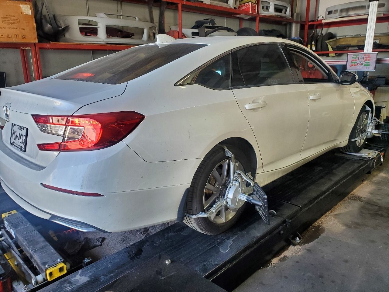 White sedan on a car lift in a garage, with wheels removed and body damage visible