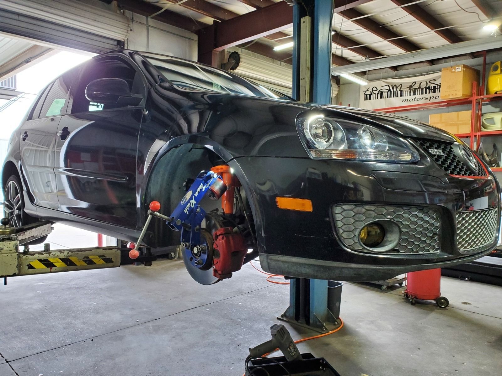 Black car lifted in a garage while a mechanic repairs the front wheel brake.