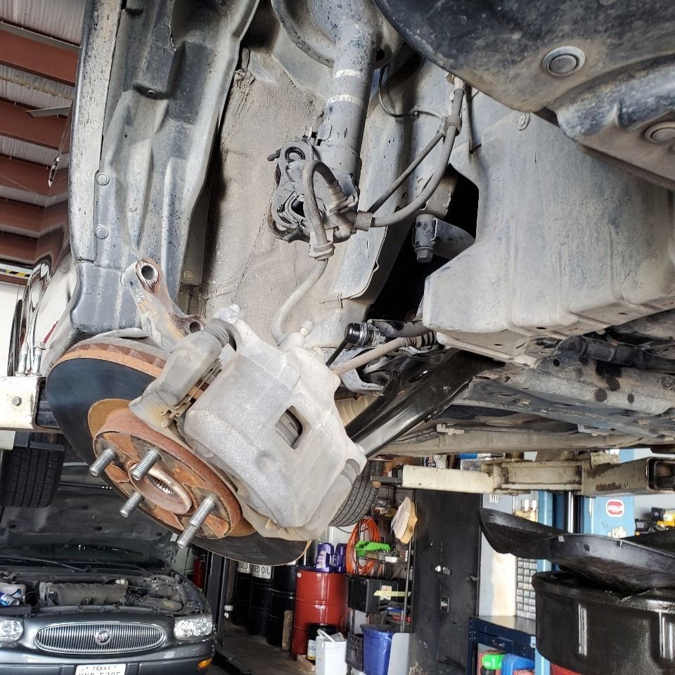 Close-up of a car’s front suspension and brake assembly on a lift in an auto repair shop.