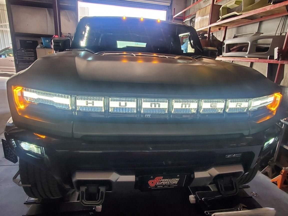 Front view of a dark truck/SUV with bright LED light bar in a garage workshop
