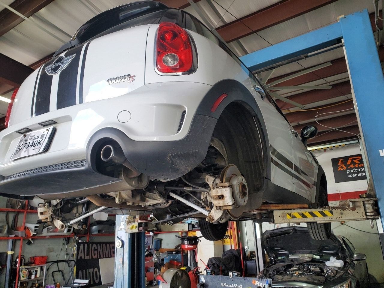 Silver Mini Cooper on a lift in an auto repair shop, with a mechanic working underneath